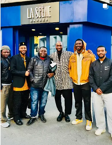 L'humoriste Bappa Oumar sur la scène du Louxor à Paris, illustrant par son geste l'union entre les cultures africaine et européenne.