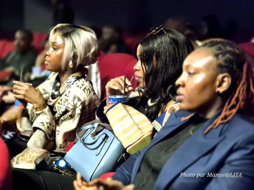 Asey Akpawa brandit le trophée du Prix du Public au nom de la réalisatrice d'Onobiren, absente ce soir :<br />
devant l'affiche de la 13e édition du Nollywood Week Film Festival.